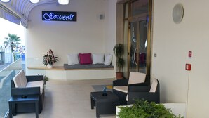A modern outdoor seating area with wicker furniture, a neon sign, and potted plants. - Hotel Souvenir (Jesolo)
