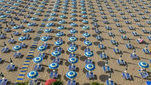 A beach with rows of sunbeds and umbrellas, a lifeguard tower, and palm trees. - Hotel Souvenir (Jesolo)