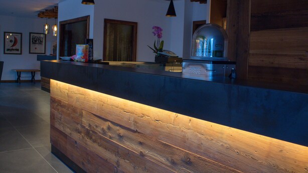 A reception area with a wooden reception desk, pendant lighting, and framed artwork on the walls. - Edelweiss Alpine Nature Hotel (Pinzolo)