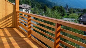 A wooden balcony with a view of a mountainous landscape, including a church and residential buildings. - Edelweiss Alpine Nature Hotel (Pinzolo)