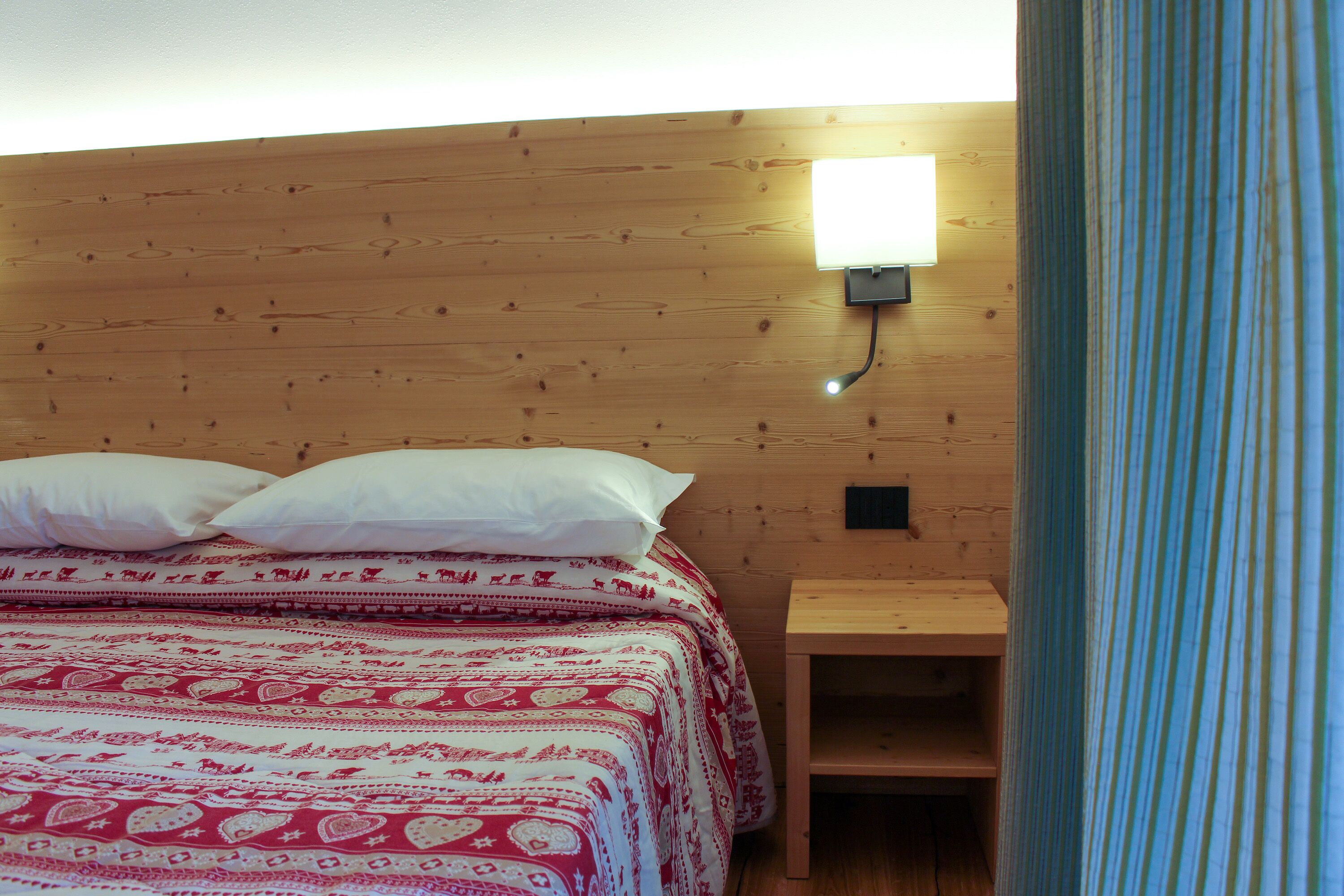 Een houten kamer met een bed, kussens en een nachtkastje.