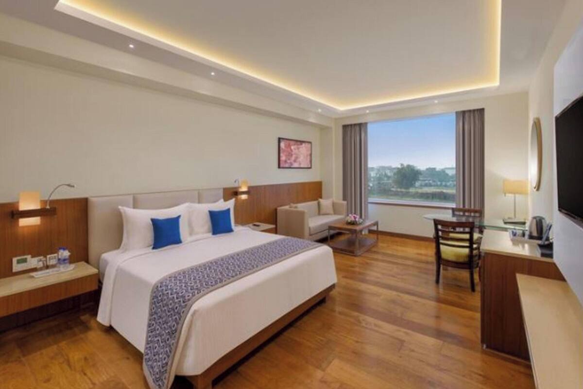 Habitación de hotel con una cama grande, un escritorio, una silla, un televisor y vistas al exterior.