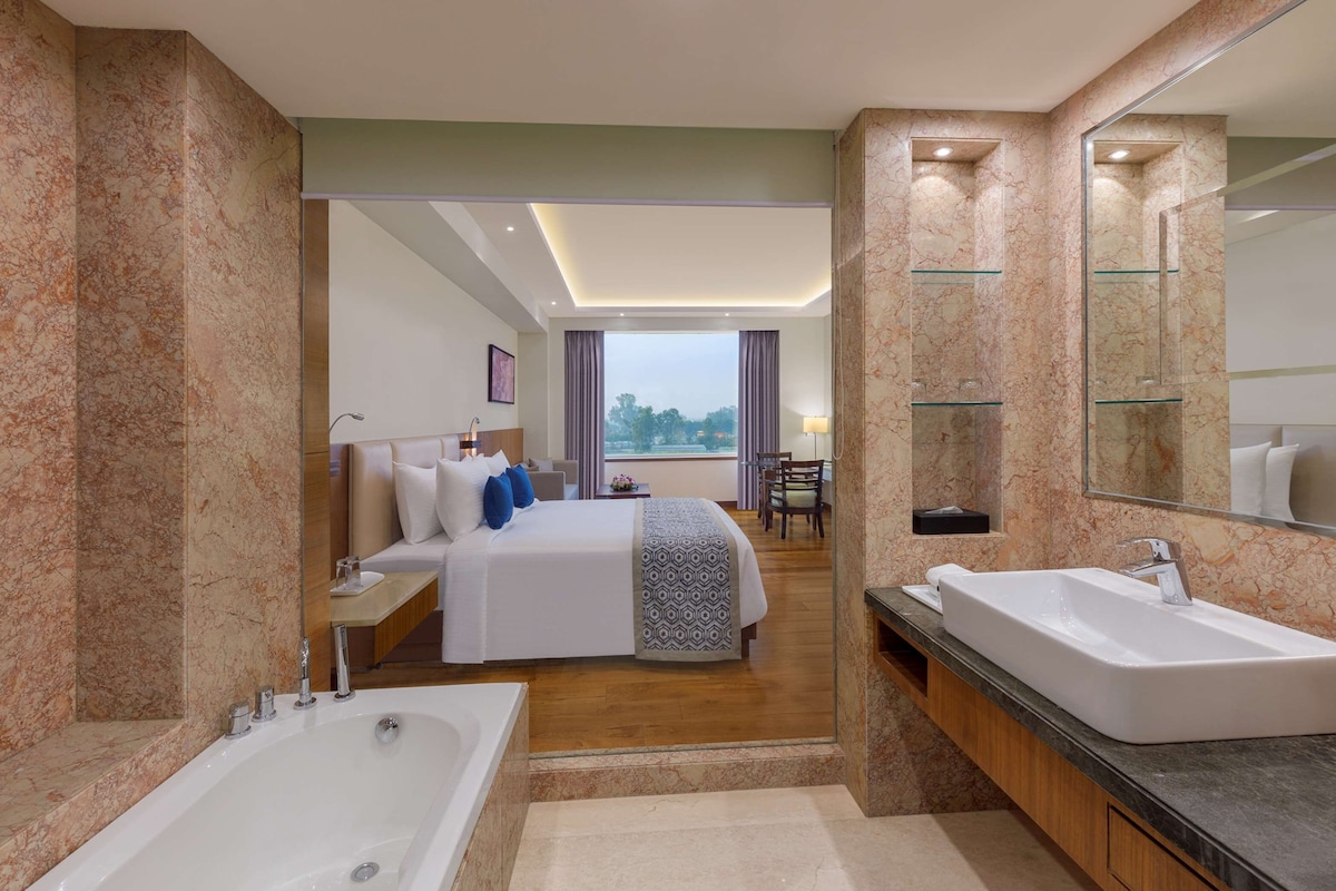 Una habitación de hotel moderna con una cama grande, un baño separado con lavamanos doble y un balcón con vistas.