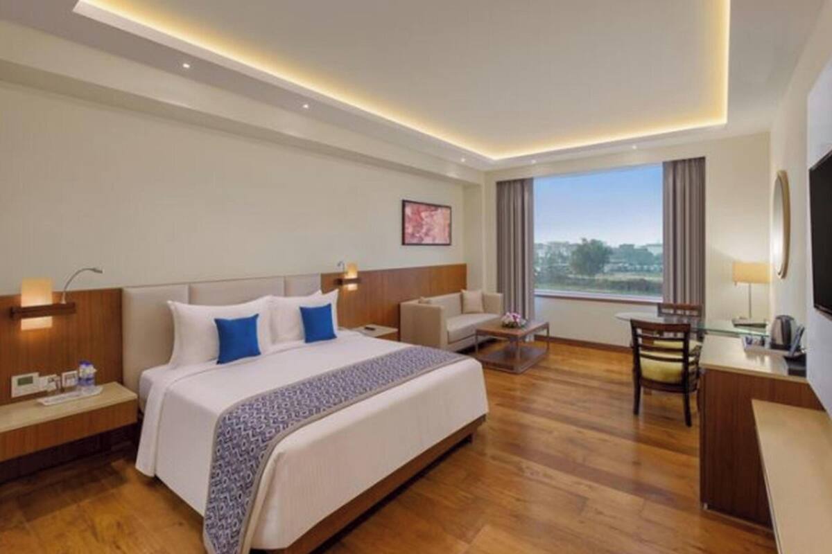 Una habitación de hotel con una cama grande, un escritorio, una silla, un sofá y vistas al exterior.
