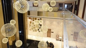 Vestíbulo de hotel de varios niveles con barandilla de vidrio, luminarias esféricas decorativas y piso de mármol.