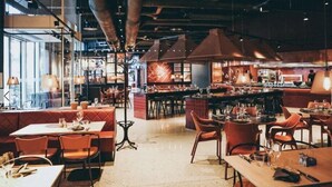 Un restaurante moderno con techos altos, conductos expuestos y una variedad de arreglos de asientos, incluyendo cabinas y mesas.