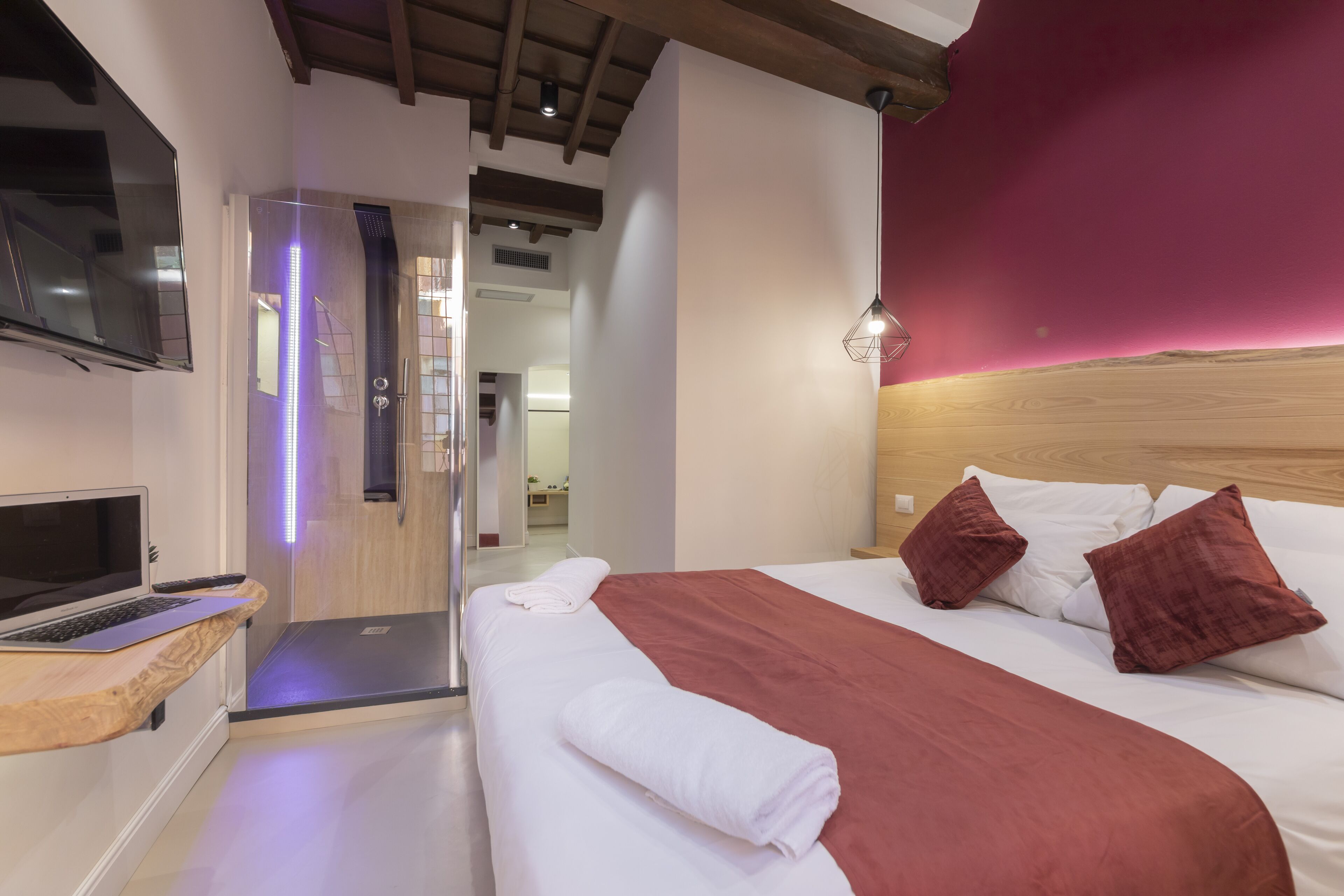 Ein Hotelzimmer mit Bett, Fernseher, Laptop und Duschbereich.