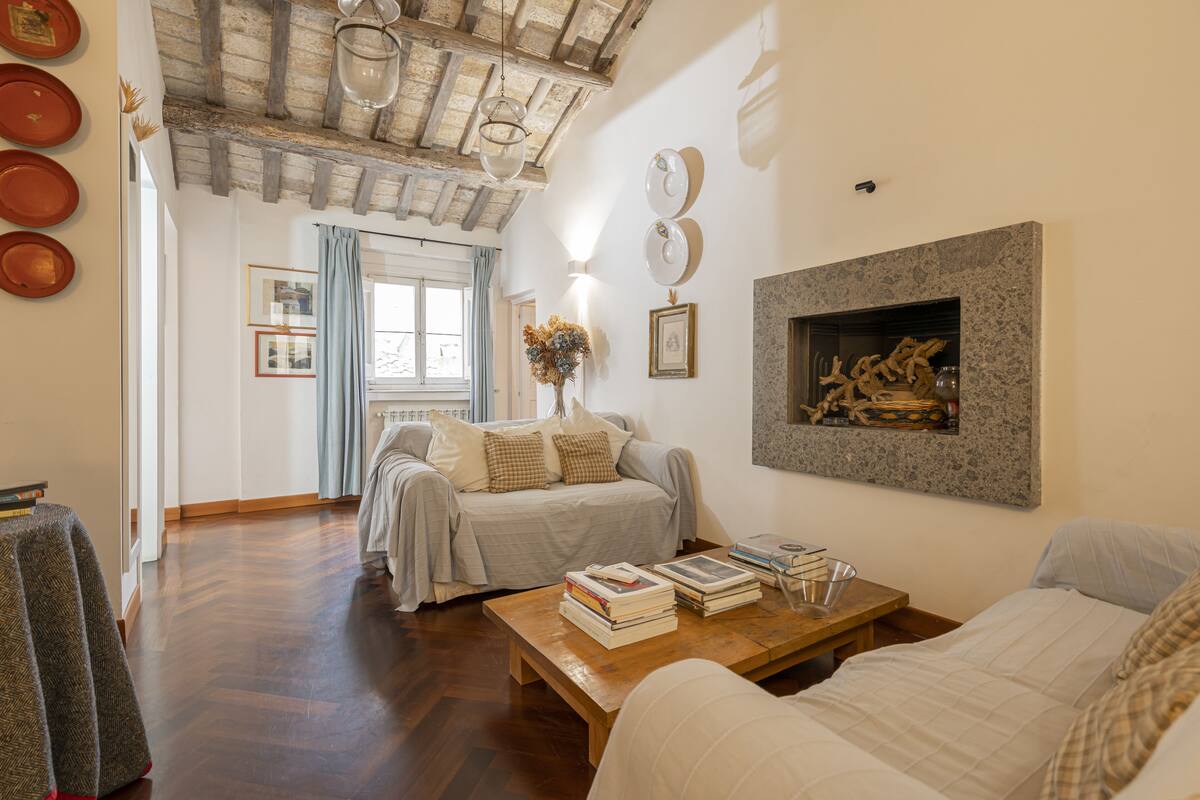 A spacious living room with a wooden floor, a sofa, a coffee table with books, and a fireplace.