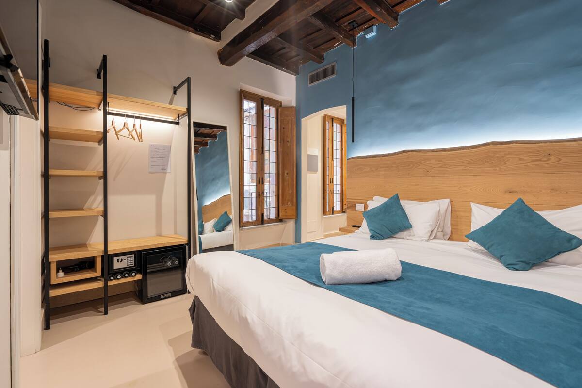 A bedroom with a large bed, a wooden headboard, a built-in wardrobe, and a small kitchenette.