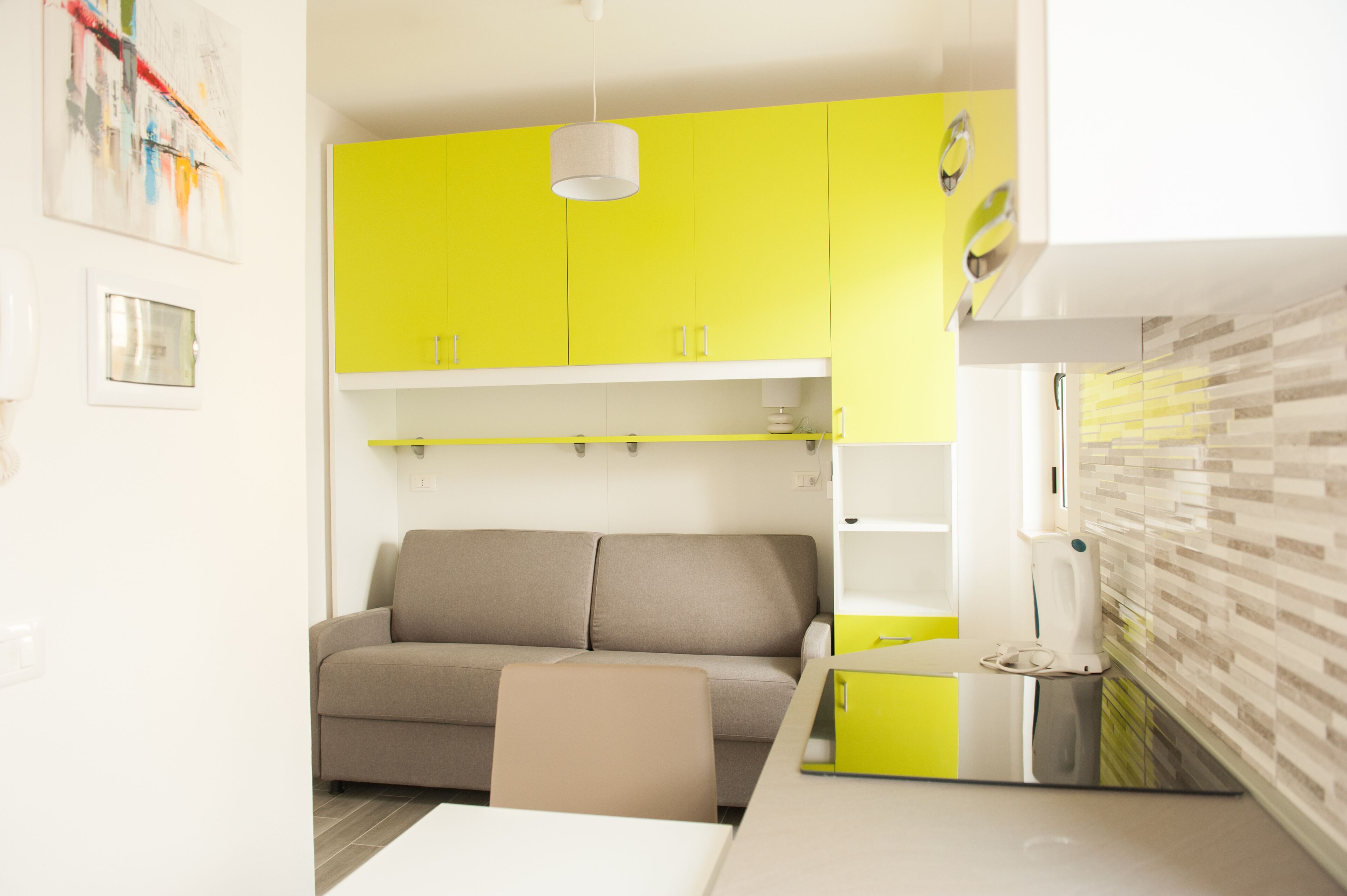 Eine moderne Küche mit leuchtend gelben Schränken, einem grauen Sofa und einem weißen Esstisch.