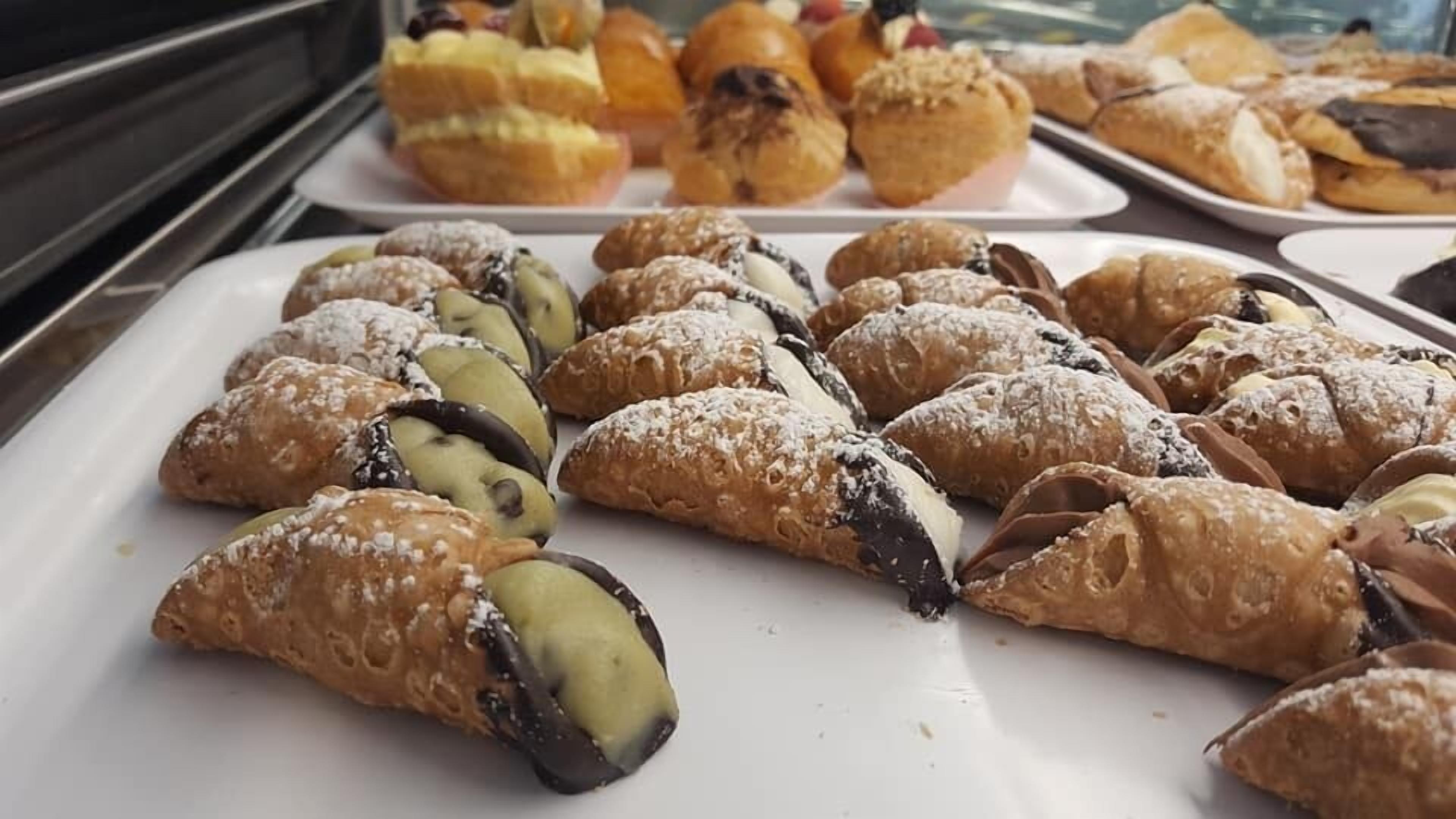 A display of assorted pastries, including cannoli and croissants, on a white tray.