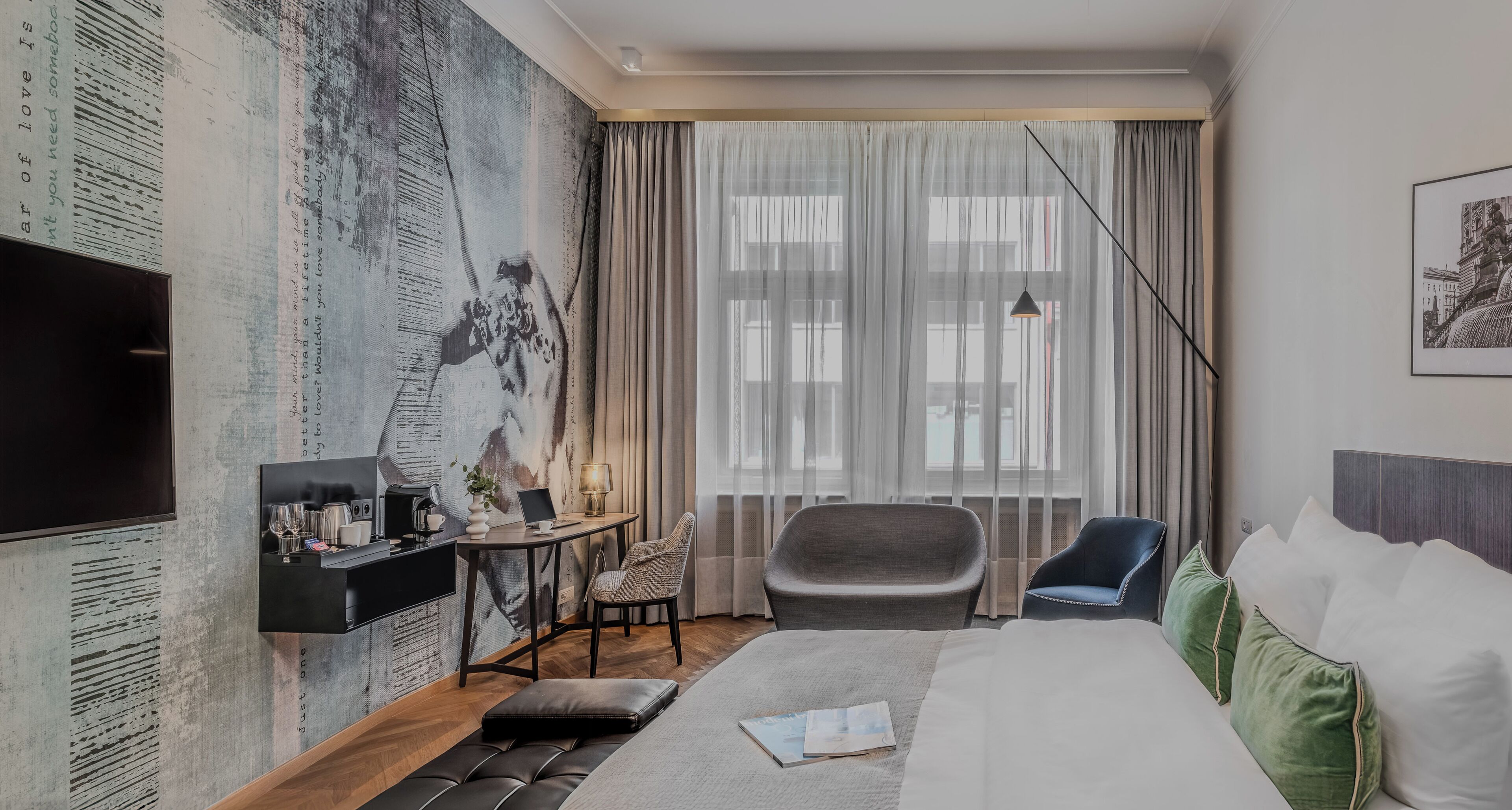 A hotel room with a bed, a desk with a computer, a chair, a TV, and a large window with curtains.