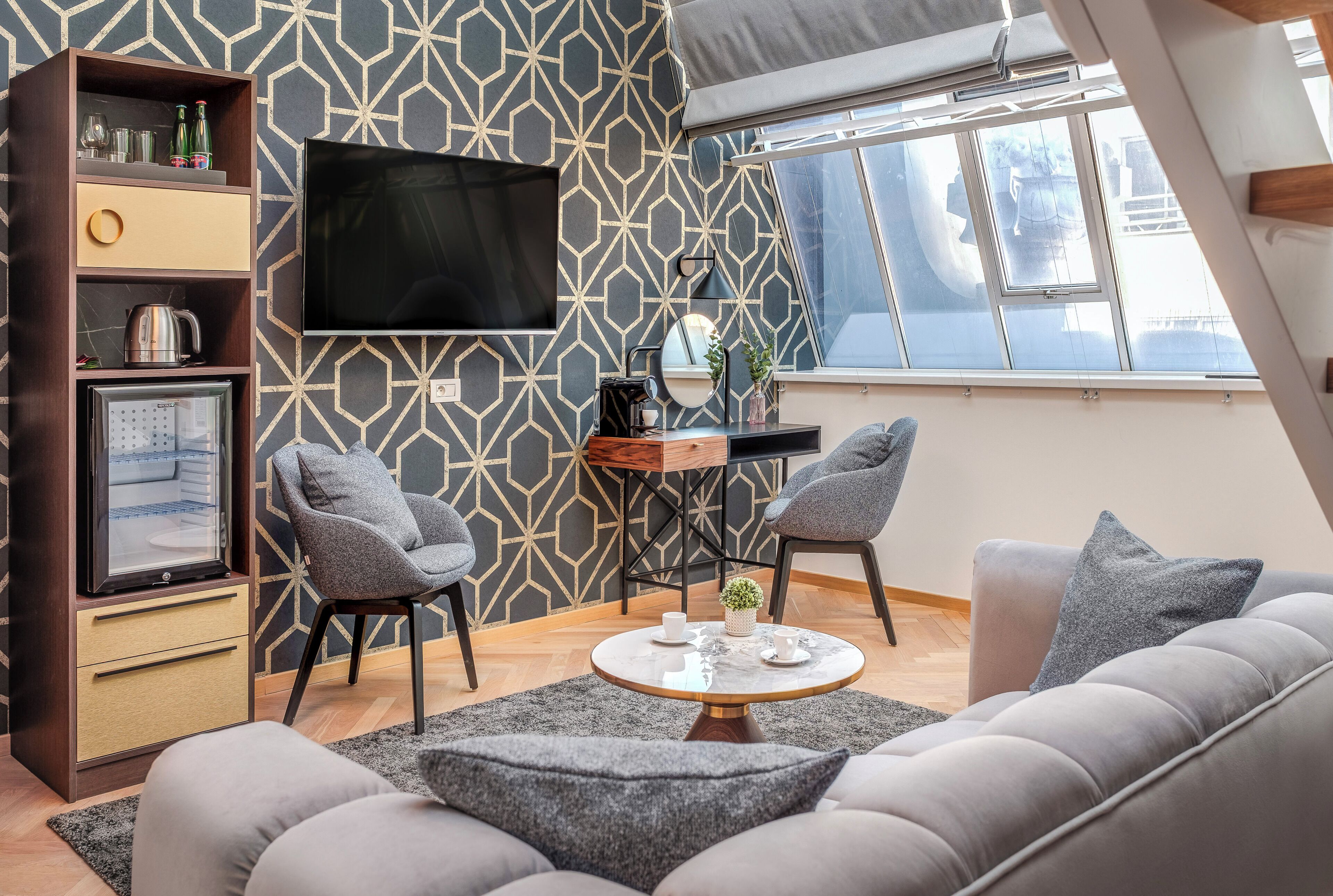 A modern living room with a sofa, two armchairs, a coffee table, a TV, and a bookshelf.
