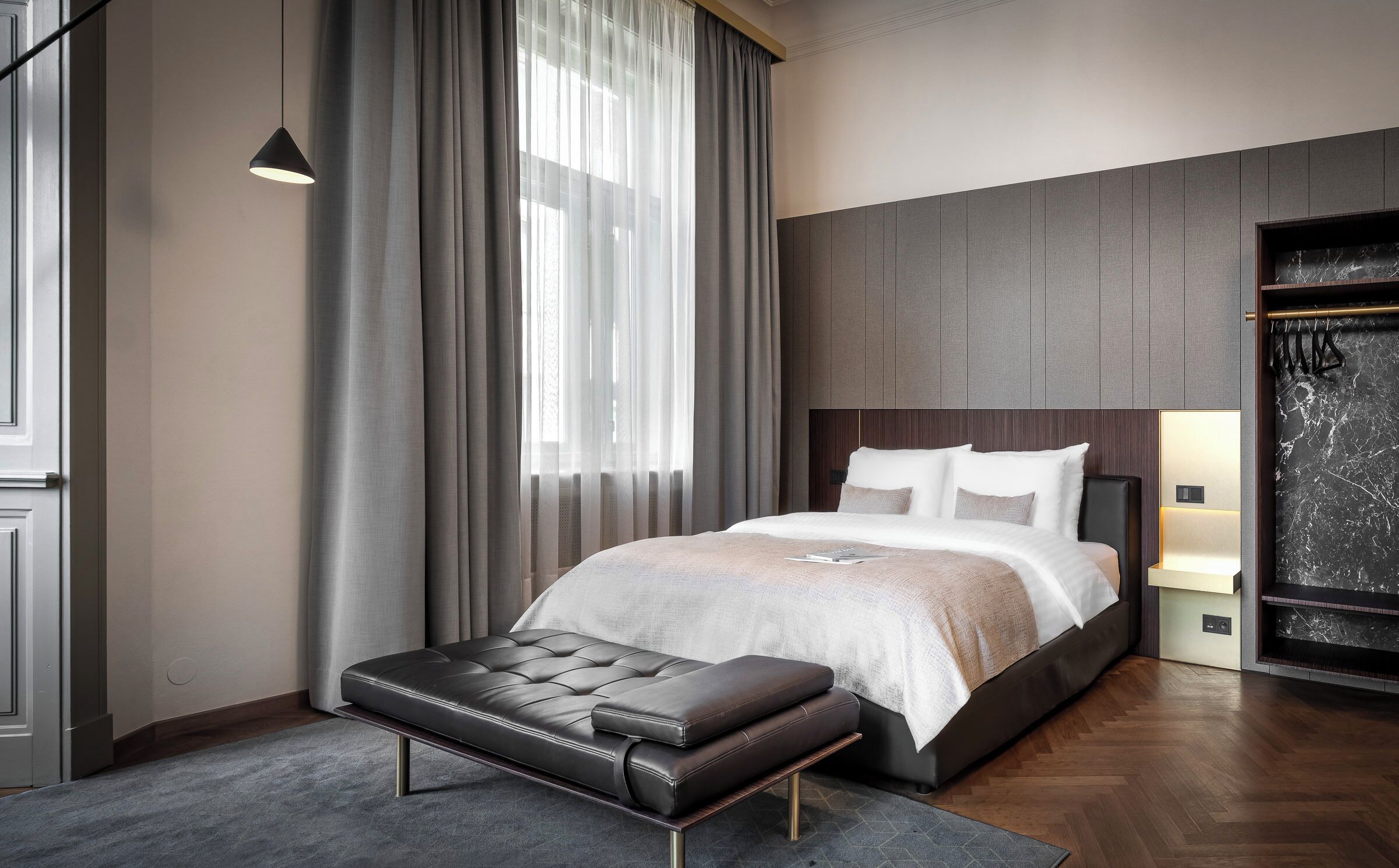 A modern bedroom with a large bed, a bench, and a wardrobe.