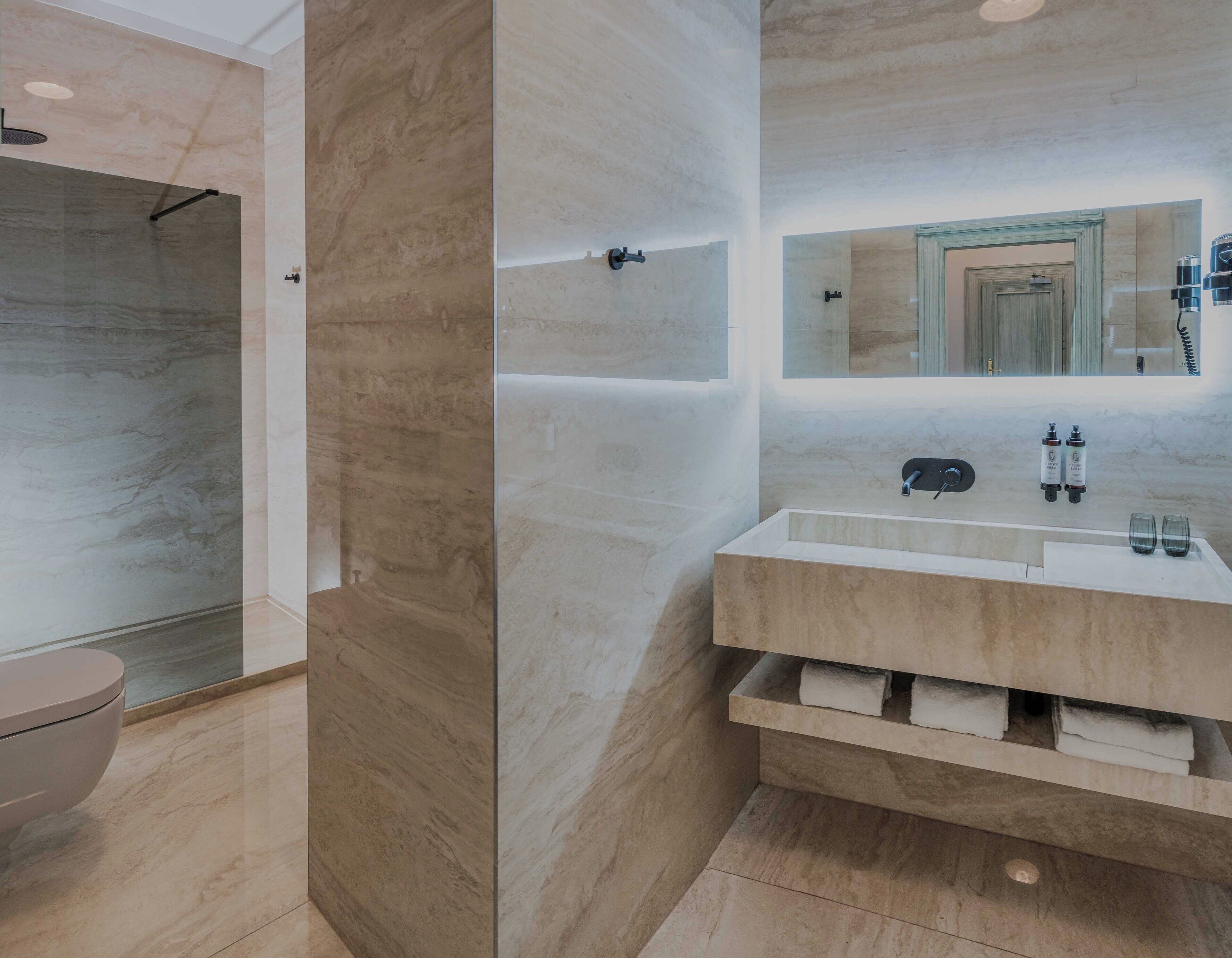 Un baño moderno con ducha de mármol, un espejo grande y un tocador con lavabo y espacio para toallas.