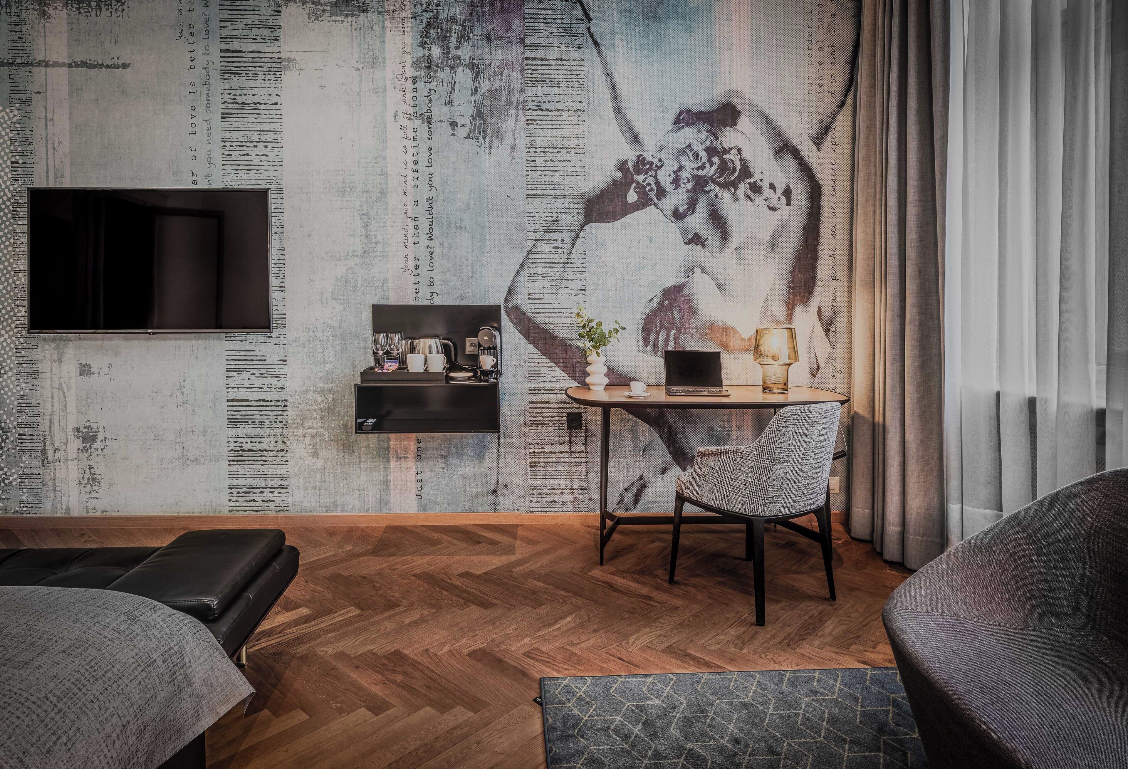 A modern room with a herringbone floor, a sofa, a dining table with chairs, a TV mounted on the wall, and a decorative mural.