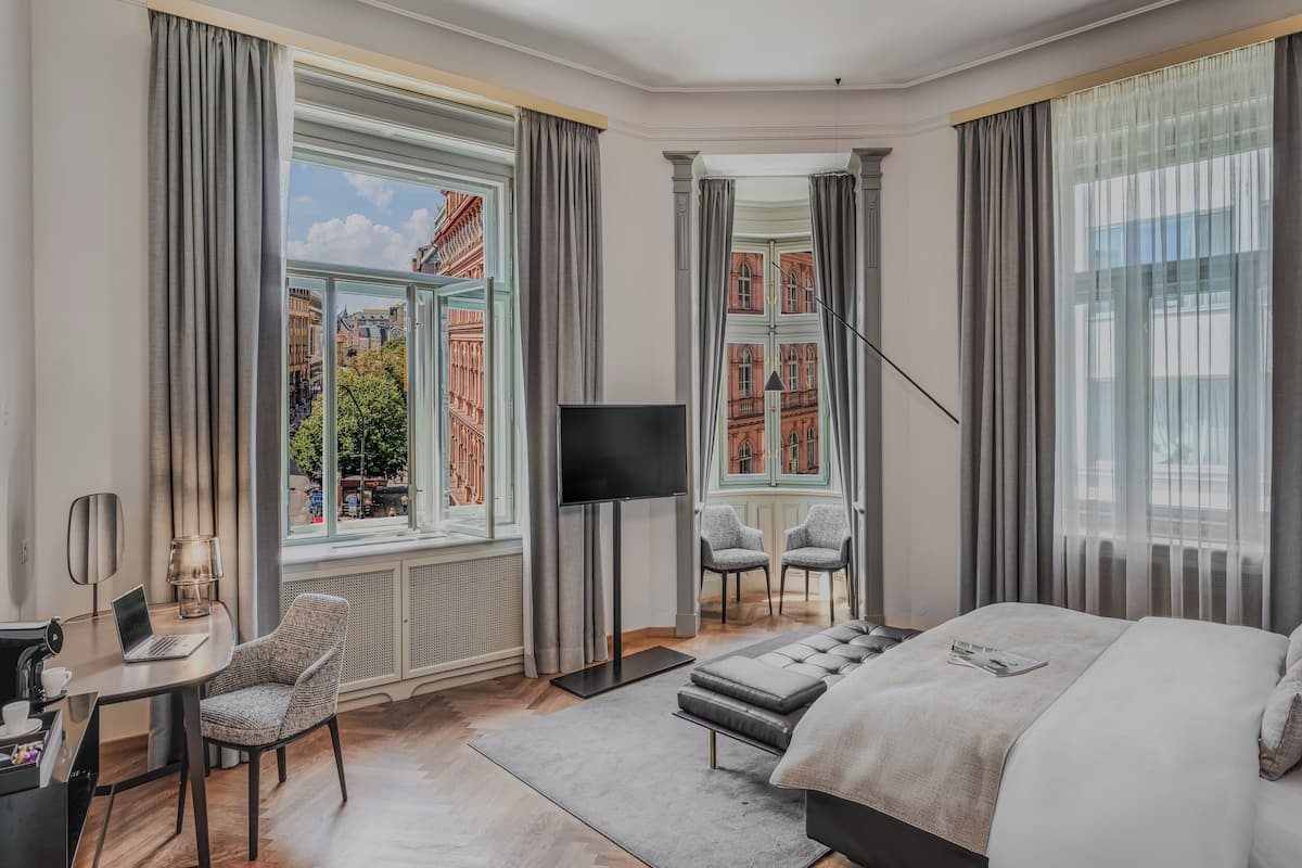 A hotel room with a large bed, a desk with a laptop, a TV, and two chairs.
