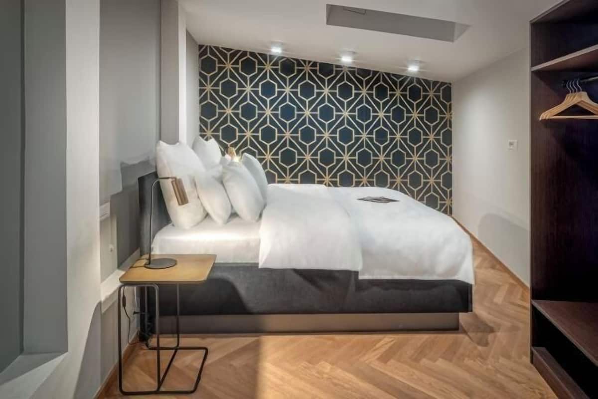 A bedroom with a bed, bedside table, and a patterned wall.
