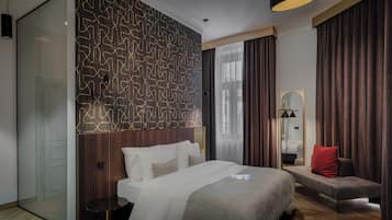 A hotel room with a large bed, a seating area, a mirror, and a patterned wall.
