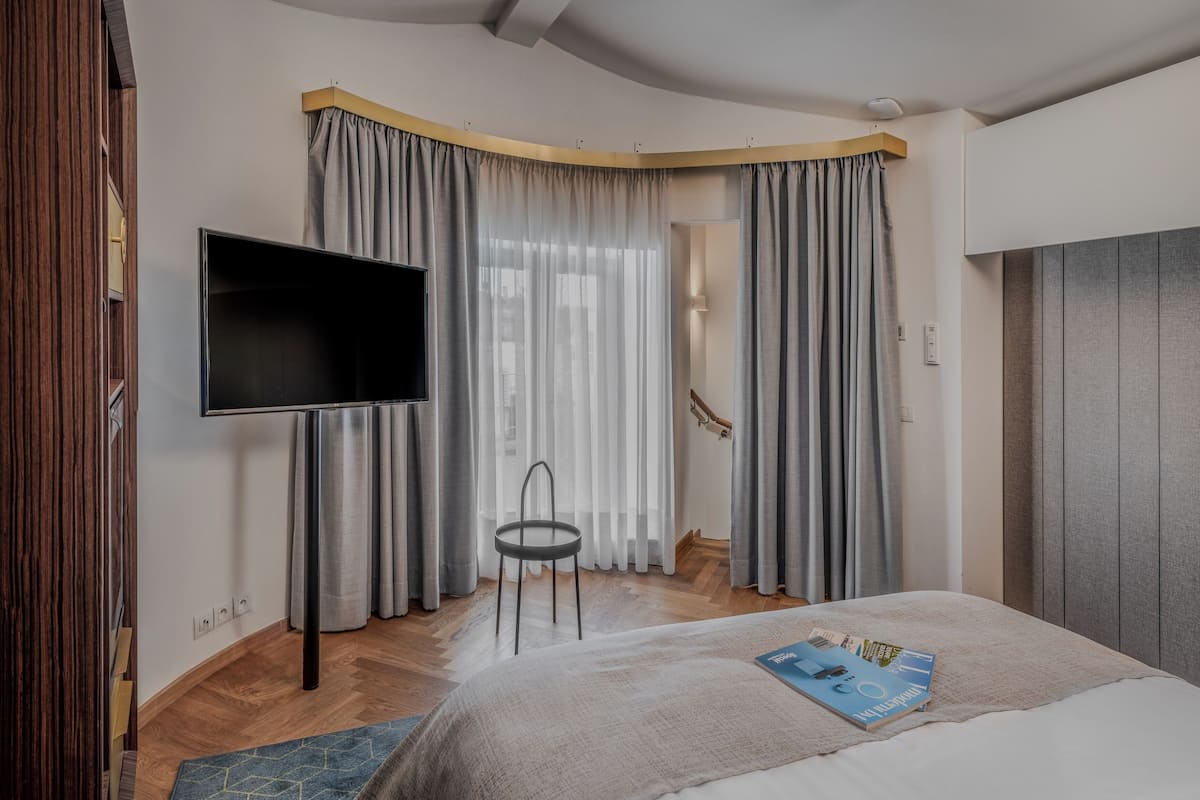 A modern bedroom with a flat-screen TV, a bed with a magazine, and a chair.