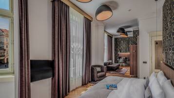 A hotel room with a large bed, a TV, a desk with a chair, and a view of the street.
