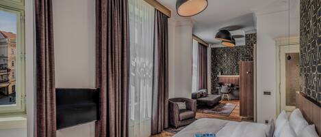 A hotel room with a large bed, a TV, a desk with a chair, and a view of the street.