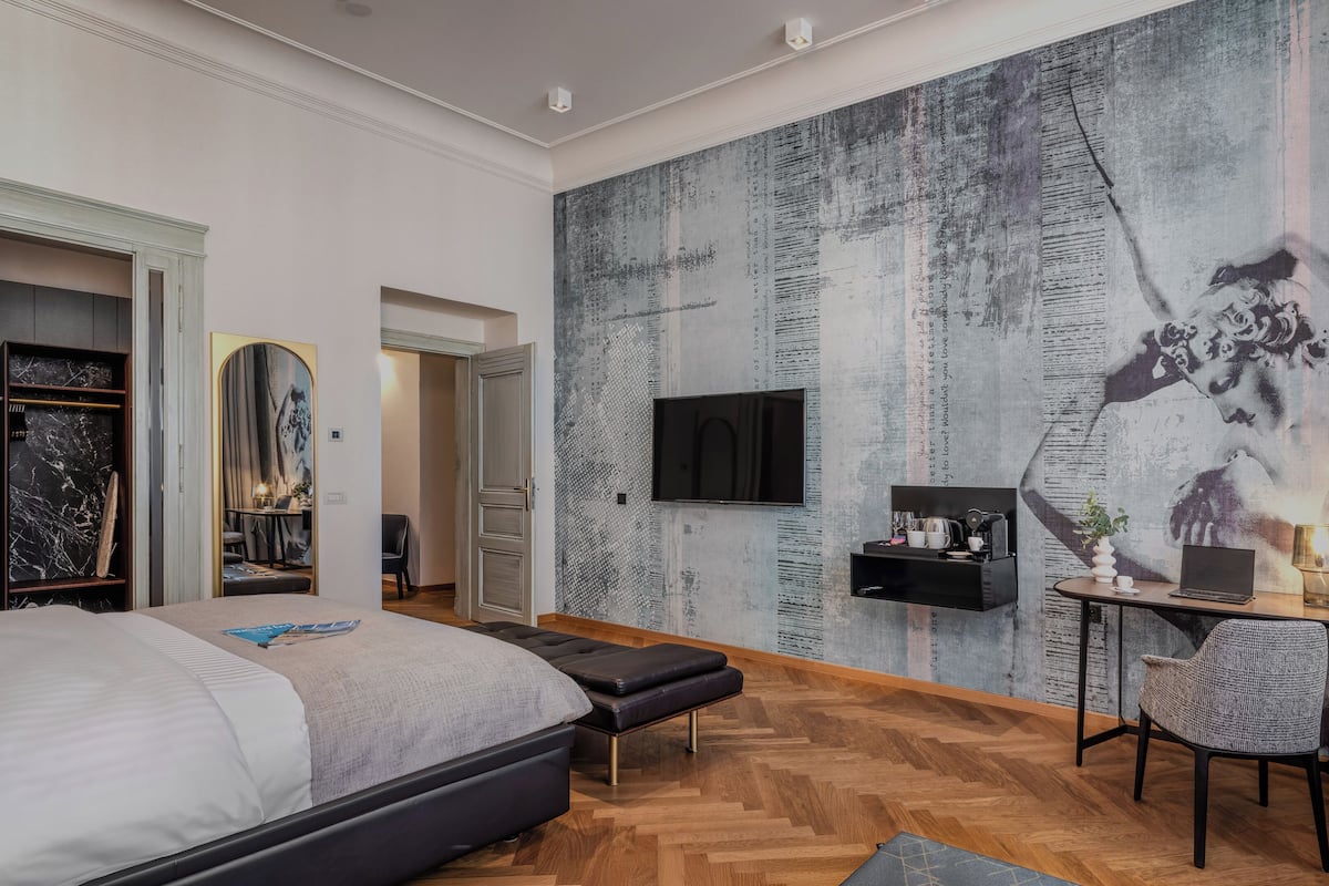 A modern bedroom with a large bed, a TV mounted on the wall, and a unique textured mural.
