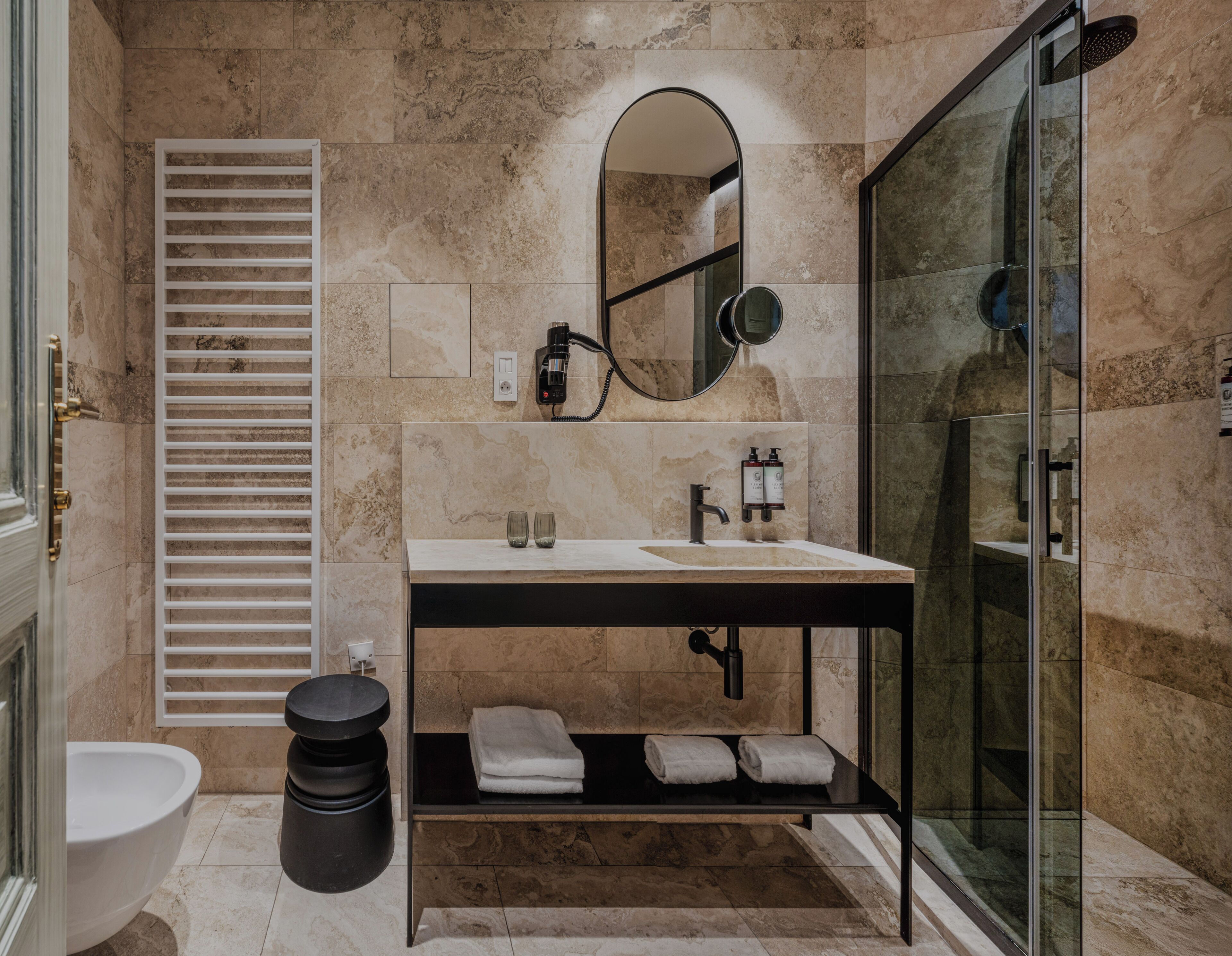 A modern bathroom with a glass shower enclosure, a white sink with a black countertop, a mirror above the sink, and a towel rack with towels.