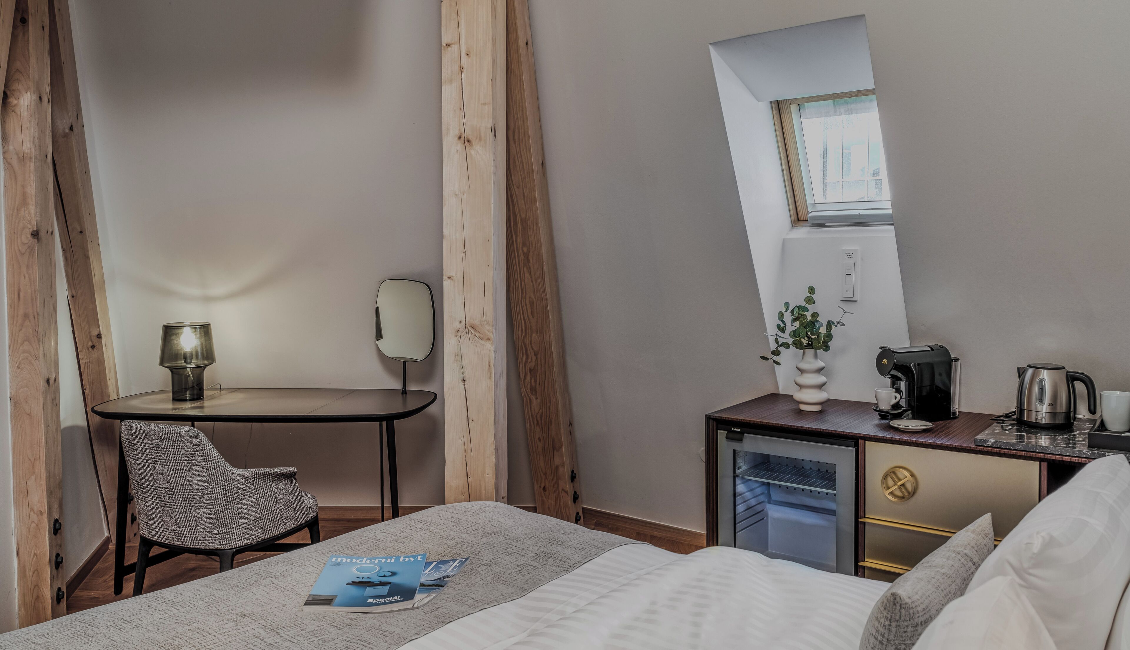 Habitación de hotel con cama, escritorio con silla, kitchenette pequeña, espejo y ventana.