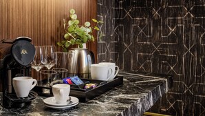 Encimera de mármol con cafetera, tazas, vasos, una bandeja con aperitivos y una planta en maceta.