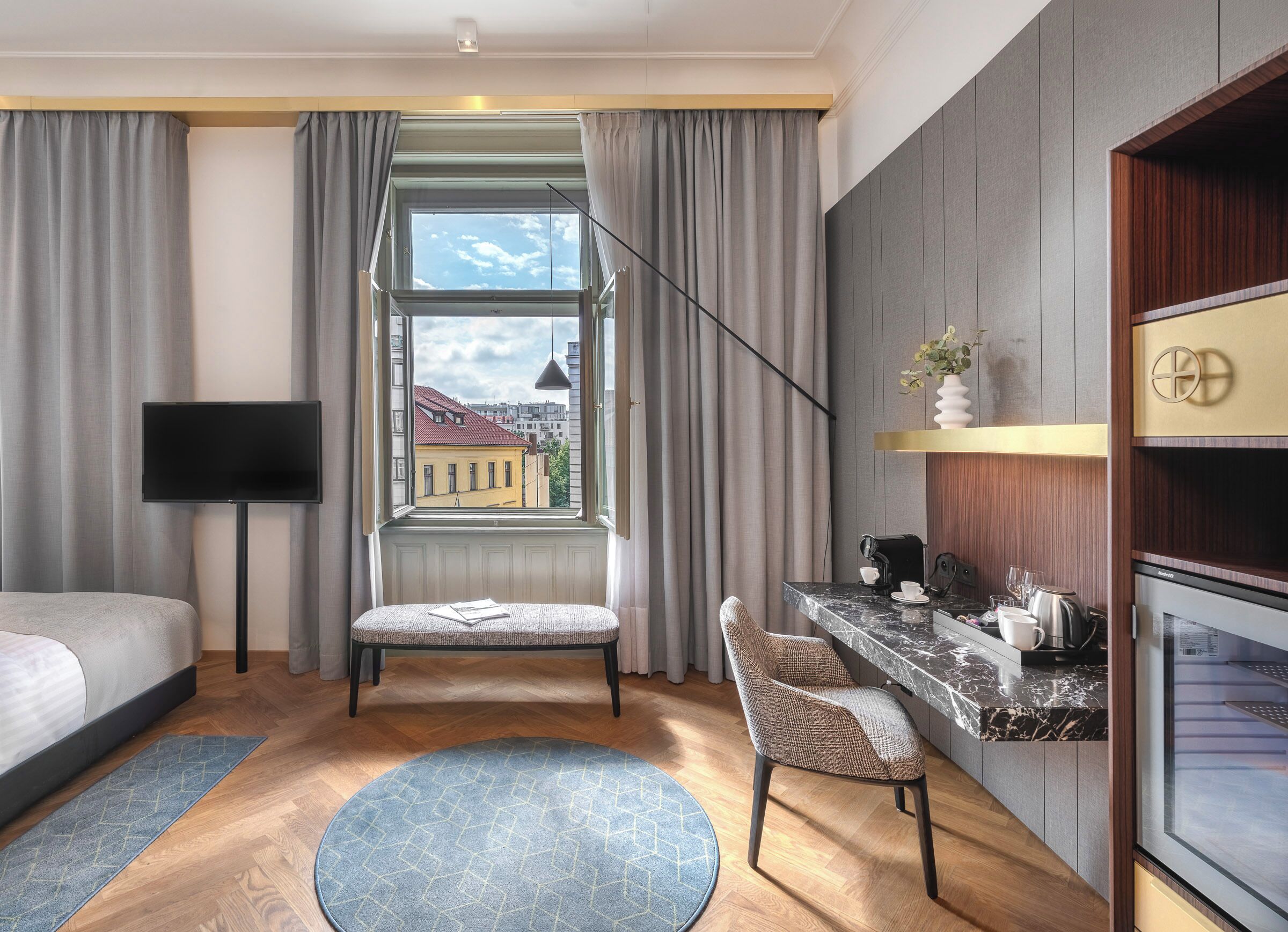 Ein modernes Hotelzimmer mit Bett, Schreibtisch mit Kaffeemaschine, Stuhl, Fernseher und einem fenster mit Vorhängen.