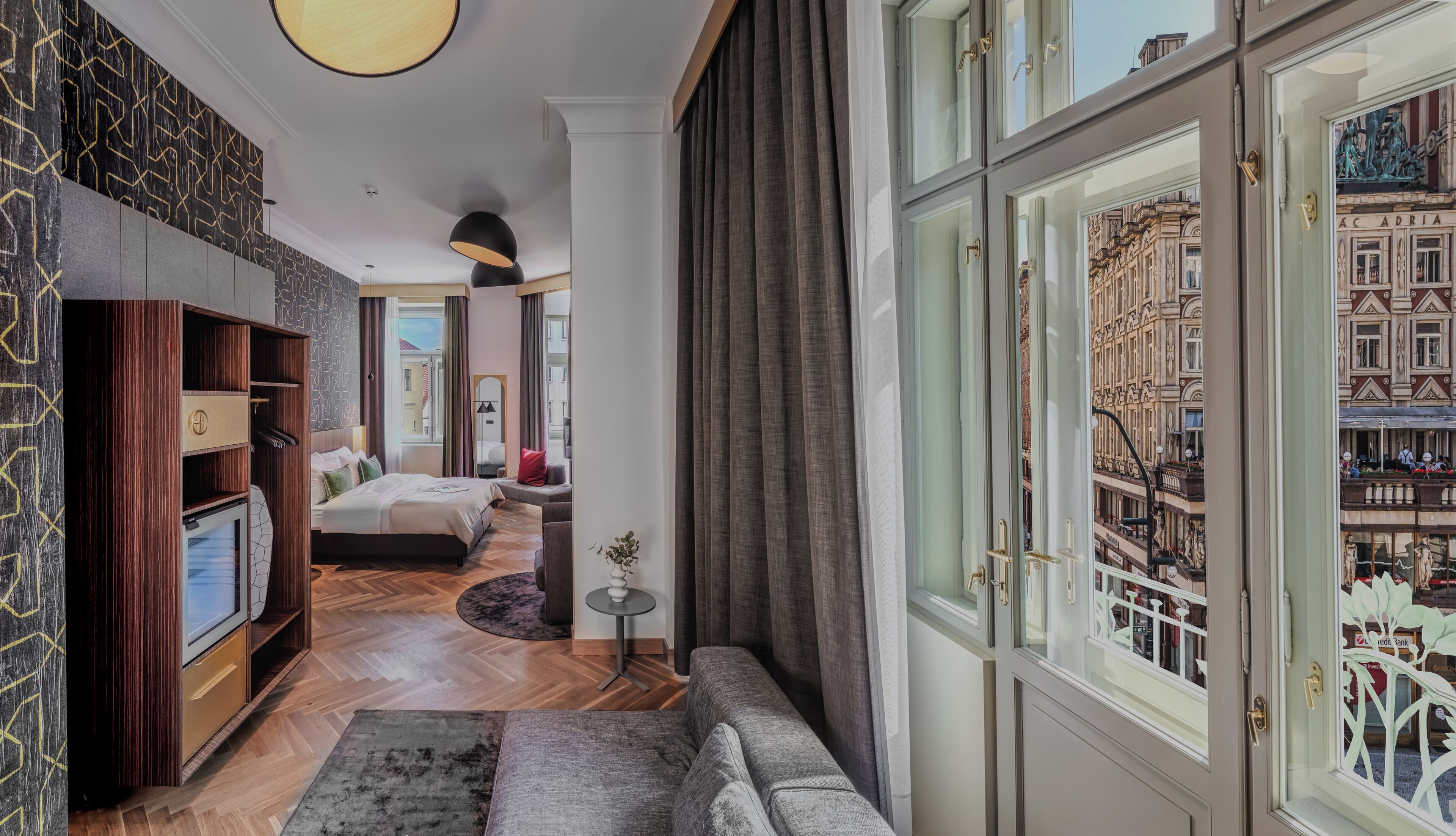 A hotel room with a large bed, a seating area, a small table, and a view of the city through a large window.