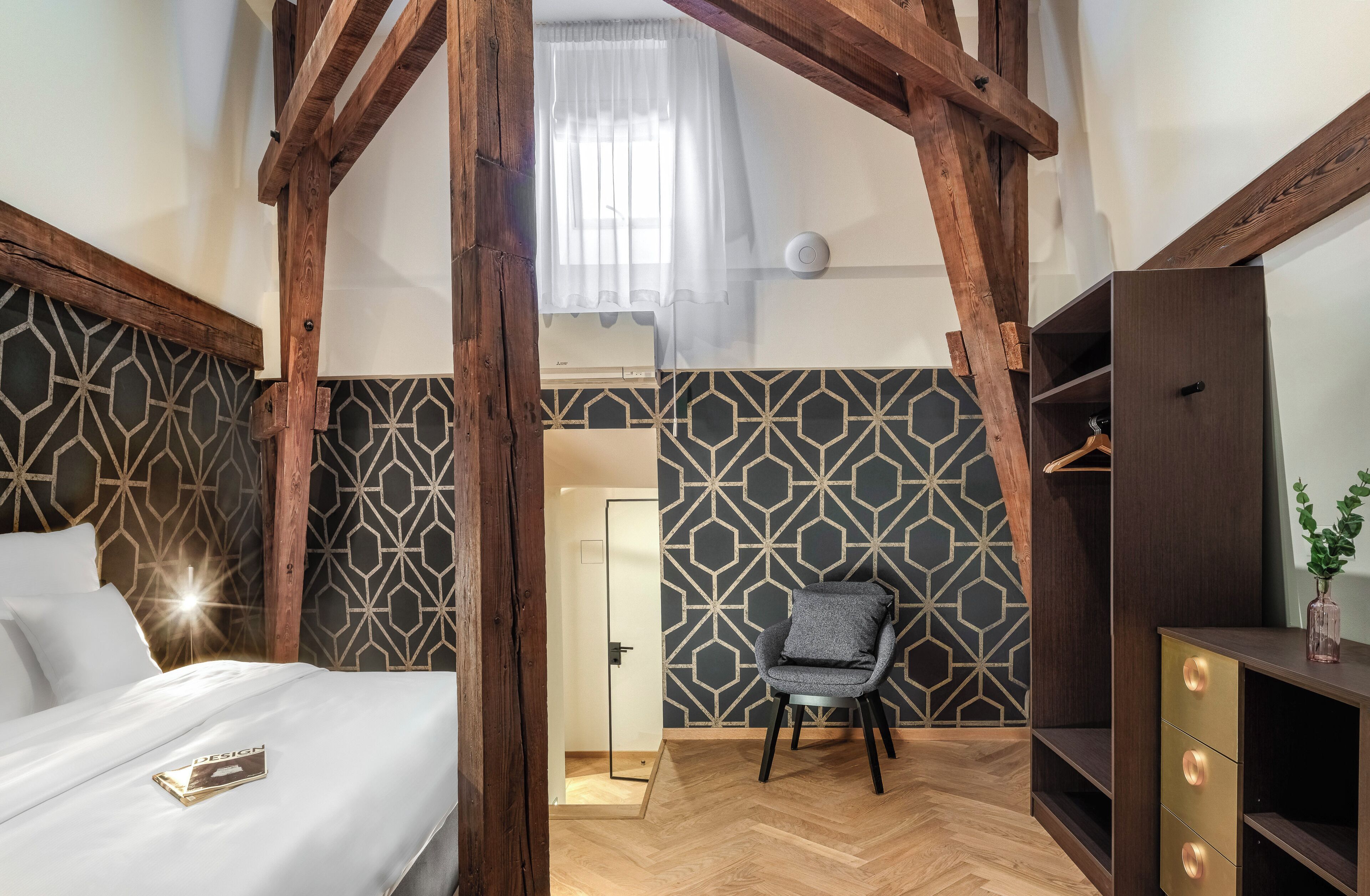 A bedroom with a bed, a chair, a dresser, and a door leading to another room.