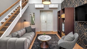 Una sala moderna con un sofá gris, una mesa de centro redonda, un sillón gris, una escalera y una pared con estampado.