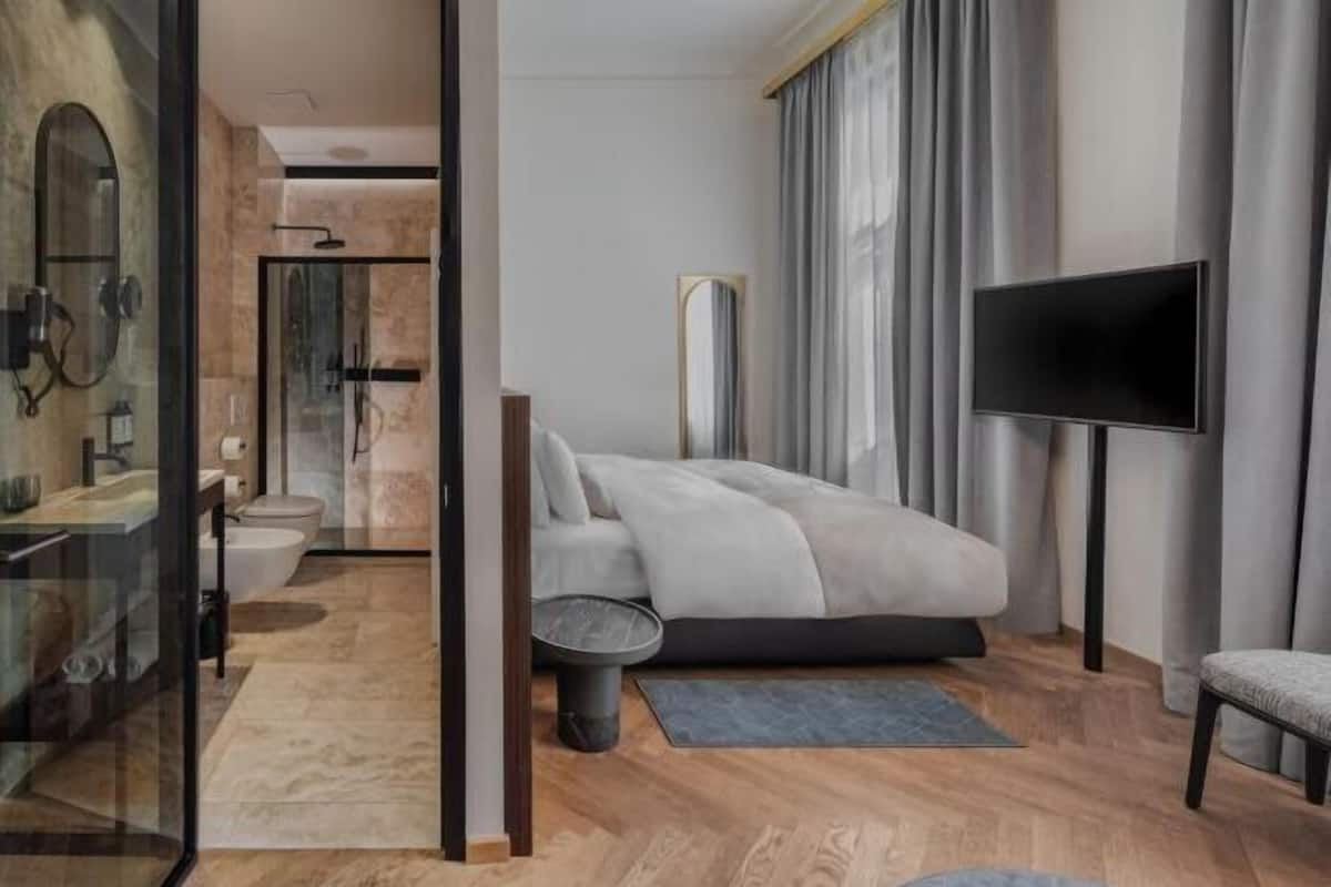 A modern bedroom with a bed, a TV, and a bathroom visible through a glass partition.