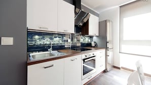 Ett modernt kök med vita skåp, en rostfri köksfläkt, en inbyggd ugn och ett stort fönster som släpper in naturligt ljus.