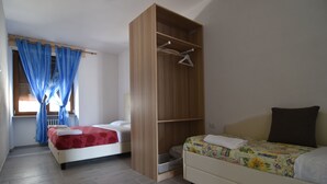 A bedroom with two beds, a wooden wardrobe, and a window with blue curtains. - Agritur Michelotti (Arco)