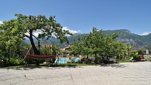 A courtyard with a hammock, a swimming pool, and mountains in the background. - Agritur Michelotti (Arco)