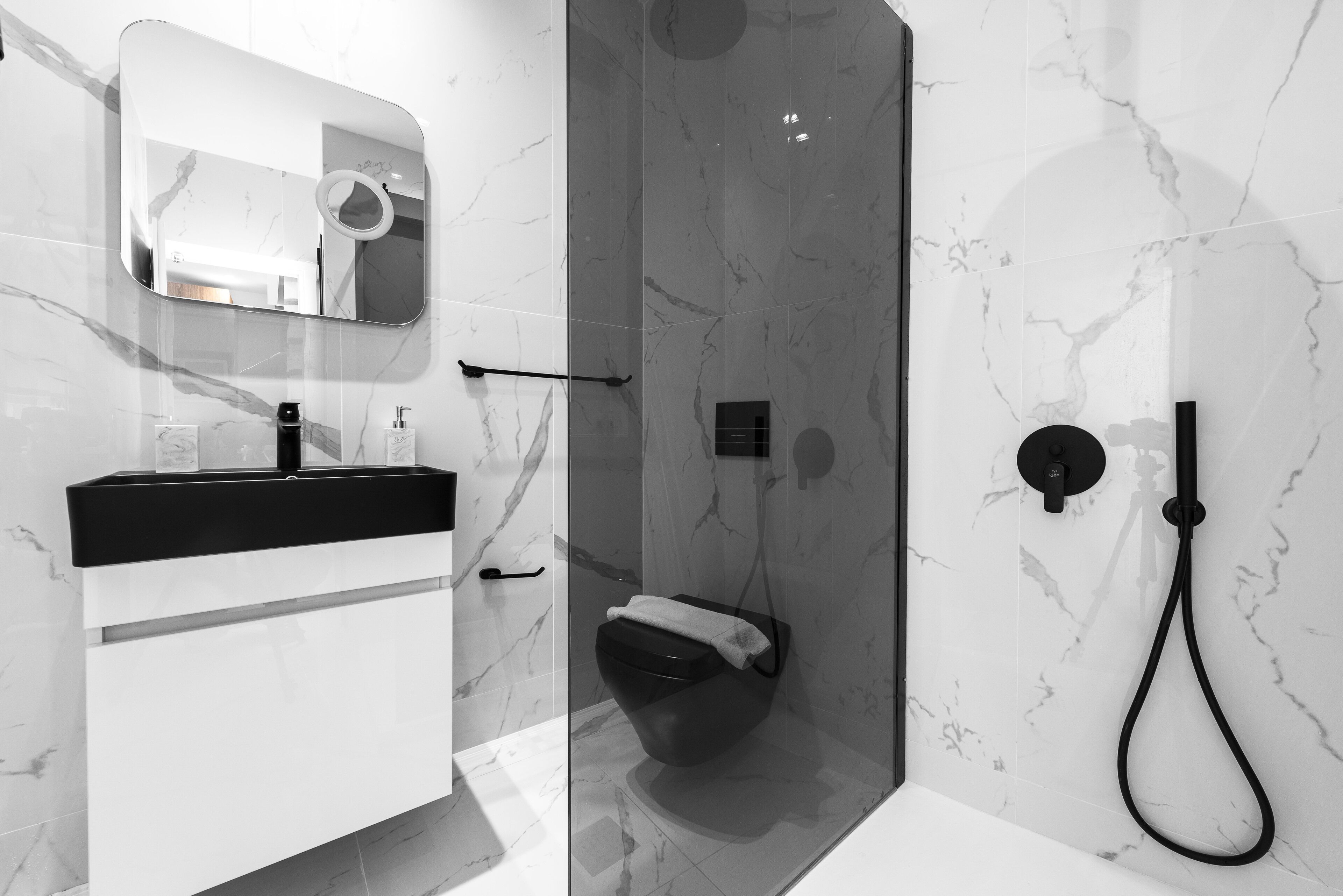 A modern bathroom with a marble wall, a black sink, and a glass-enclosed shower area.