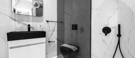 A modern bathroom with a marble wall, a black sink, and a glass-enclosed shower area.