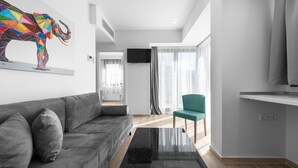 A modern living room with a gray sofa, a colorful abstract wall art, a teal chair, and a flat-screen TV mounted on the wall. - Penthouse Level 8 Nilie Hospitality MGMT (Thessaloniki)