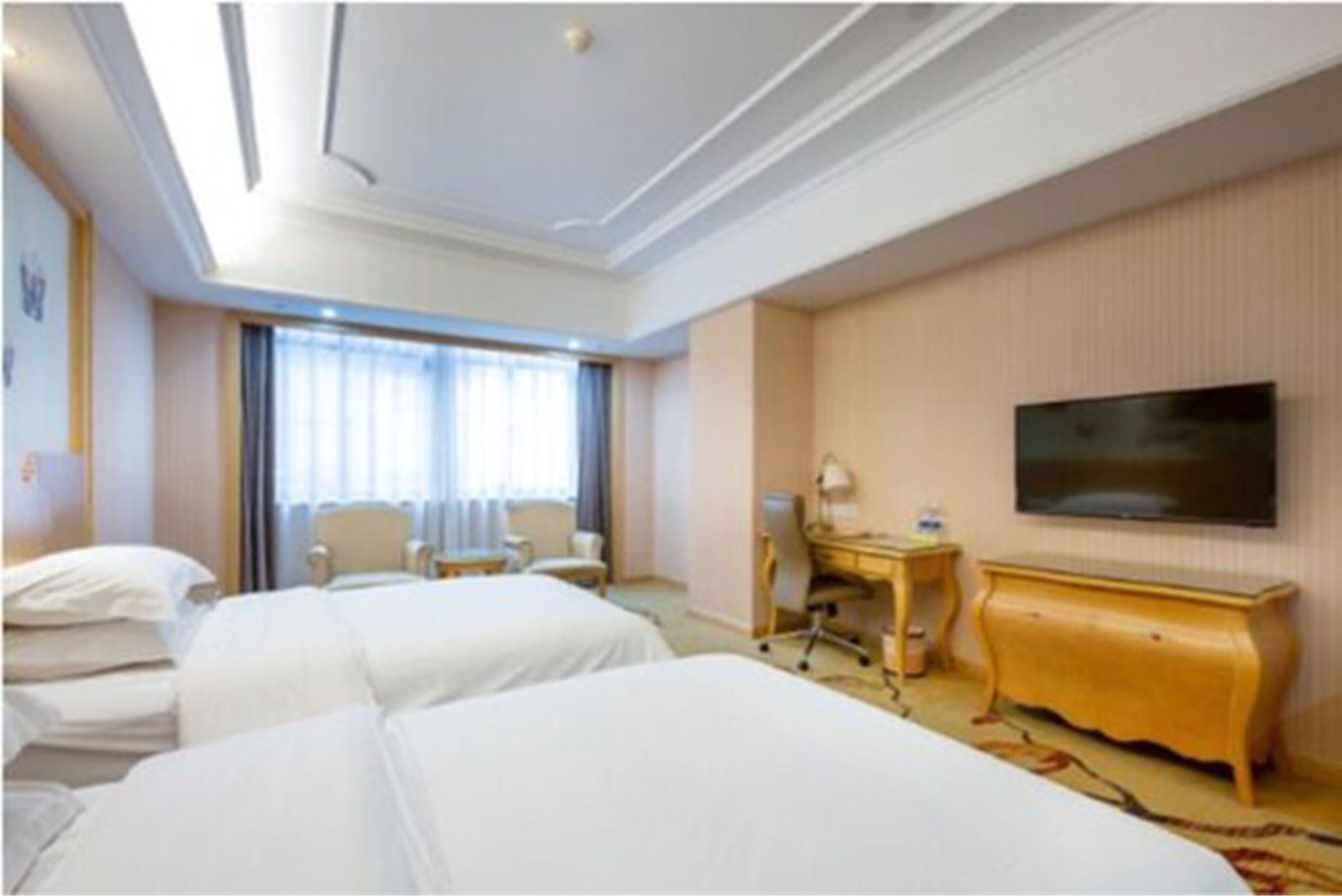 A hotel room with two beds, a desk, a chair, a TV, and a large window.