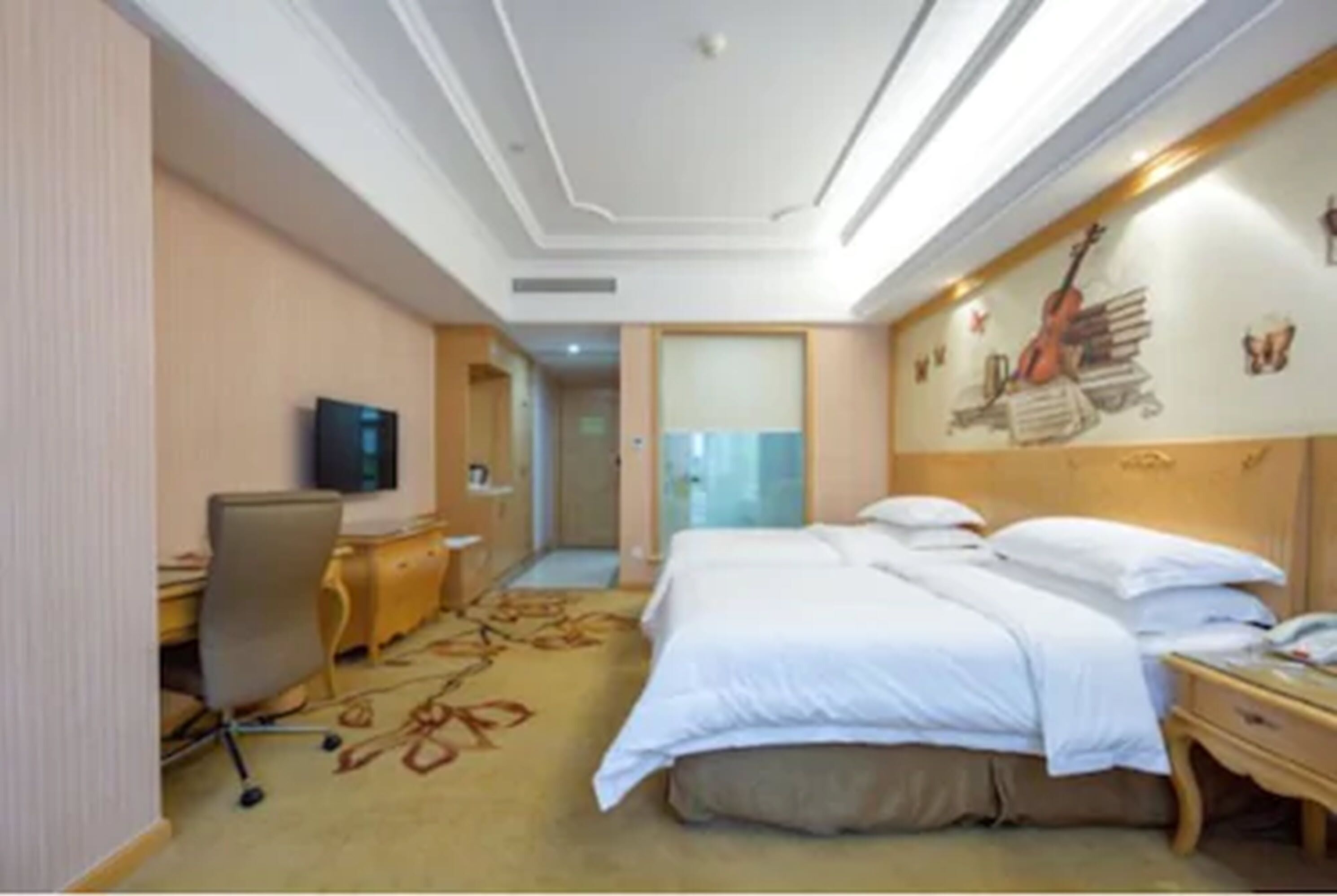 Ein Hotelzimmer mit einem Bett, einem Schreibtisch, einem Sessel, einem Fernseher und einer Wand mit einer Gitarre und Büchern.