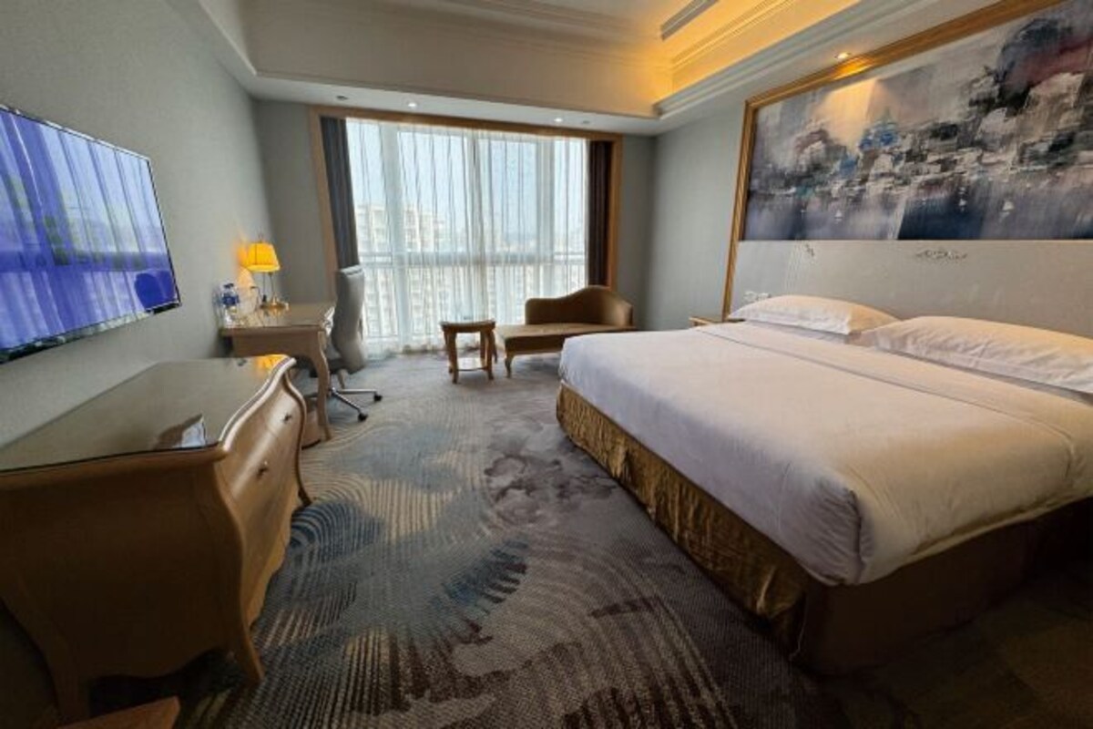 A hotel room with a bed, a desk, a chair, a television, and a large window.