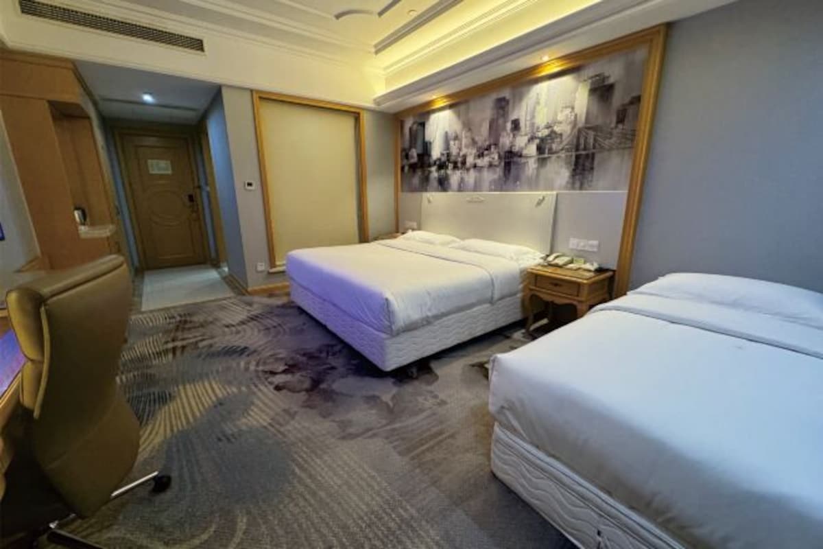 A hotel room with a large bed, a desk, a chair, and a painting on the wall.