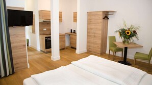 A modern hotel room with a bed, a TV, a kitchenette, and a dining area with a table and chairs. - Perkeo Apartments: Studio 3 | Heidelberg-Altstadt (Heidelberg)