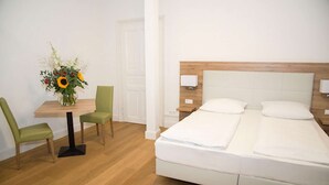 A hotel room with a bed, a desk with a chair, and a vase of flowers. - Perkeo Apartments: Studio 3 | Heidelberg-Altstadt (Heidelberg)