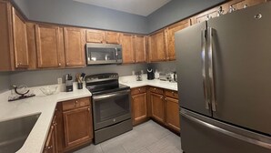 Cocina moderna con gabinetes de madera, electrodomésticos de acero inoxidable y encimera blanca.