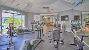 Ein Fitnessstudio mit verschiedenen Trainingsgeräten, großen Fenstern und einem Deckenventilator.