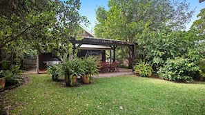 A covered patio with outdoor furniture, surrounded by lush greenery and a well-maintained lawn. - Semaphore Beach House (Hawks Nest)